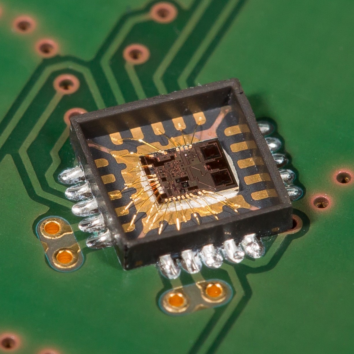 240 GHz Radar-MMIC in einem Open-Cavity-Package frü Terahertzsensorik. Die quadratischen on-Chip Antennen für den Sende- und Empfangskanal sind an der rechten Chipkante deutlich zu erkennen.  240 GHz radar MMIC in an open-cavity package for terahertz sensing. The square on-chip antennas for the transmit and receive channels are clearly visible along the right edge of the chip.
