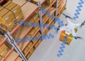 Mit RFID-Tracking Tags ausgestattete Drohne transportiert ein Paket zwischen den Ragalen eines Lagers.