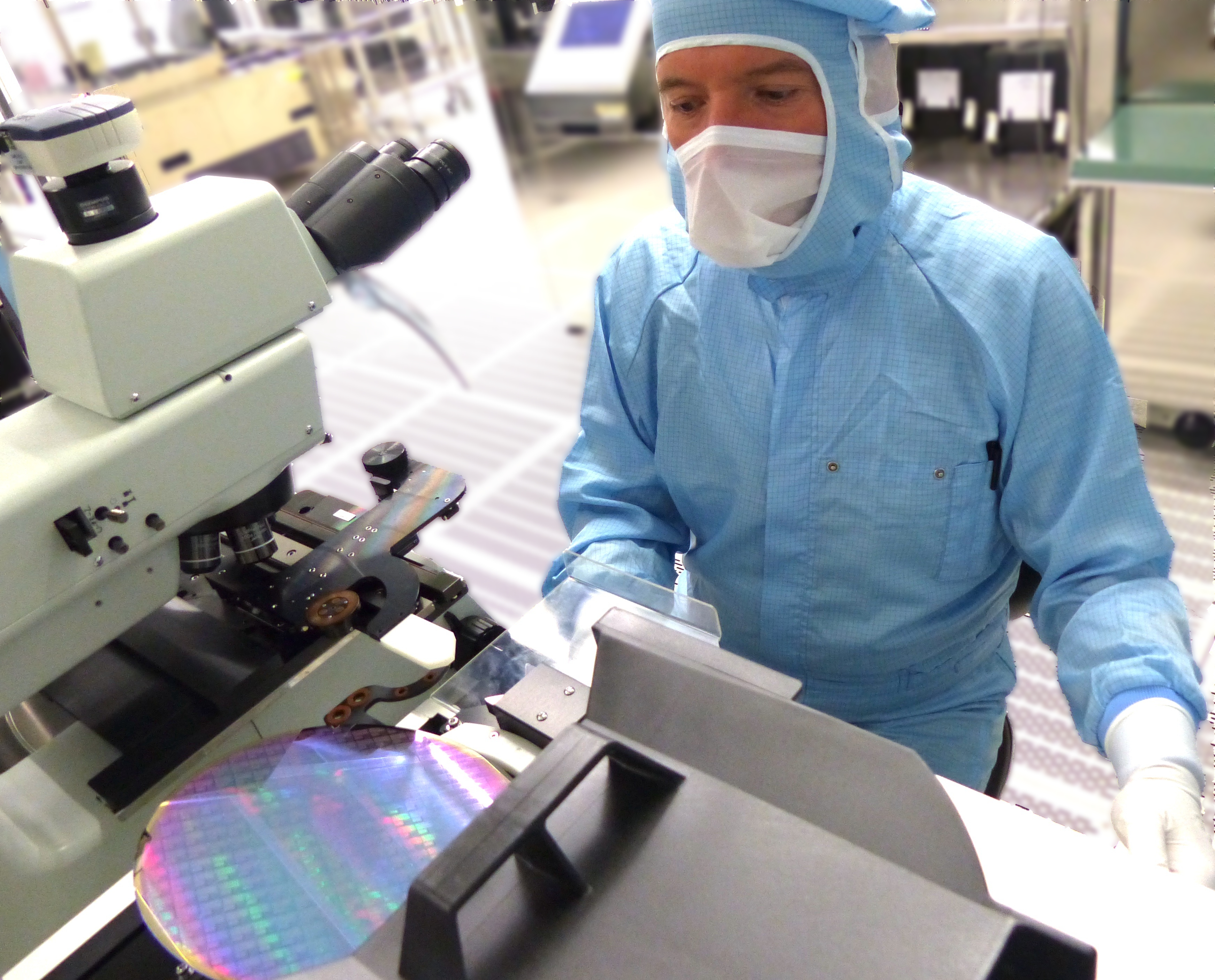 Eine Person in Reinraumkleidung bedient ein Gerät mit einem schimmernden Wafer für Terahertzsensorik. A person in cleanroom attire operates a device with a shimmering wafer for terahertz sensing.